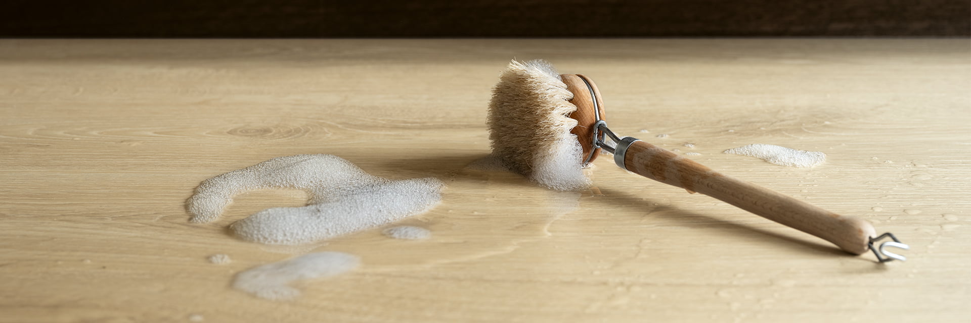 湿漉漉的清洁刷放在 Pergo 柏丽米色强化复合地板上